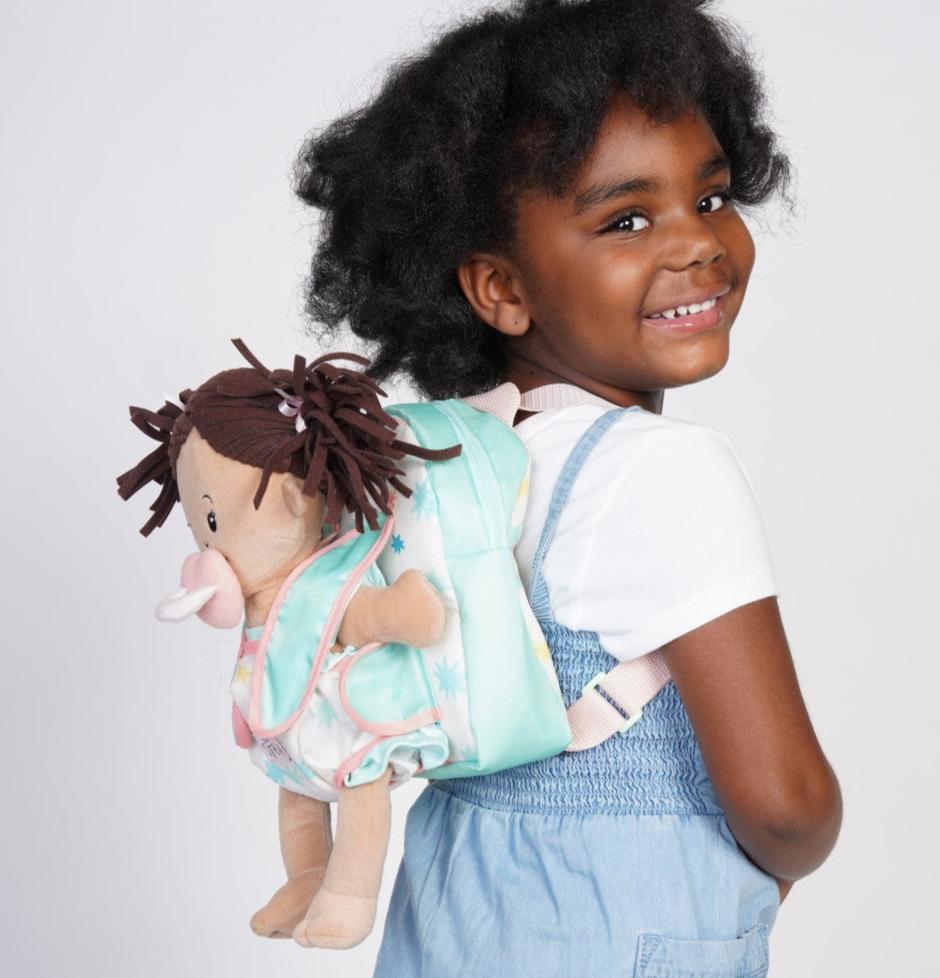 backpack carrier doll accessory with zippered pouch for storage and carrier straps on front for holding soft baby dolls being worn by a preschool age girl with a baby doll in the carrier