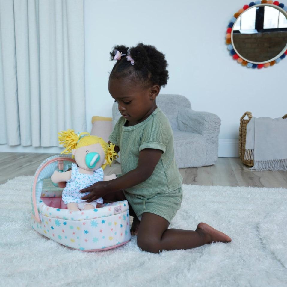 Toddler aged girl placing a soft baby doll into a soft crib in a room scene