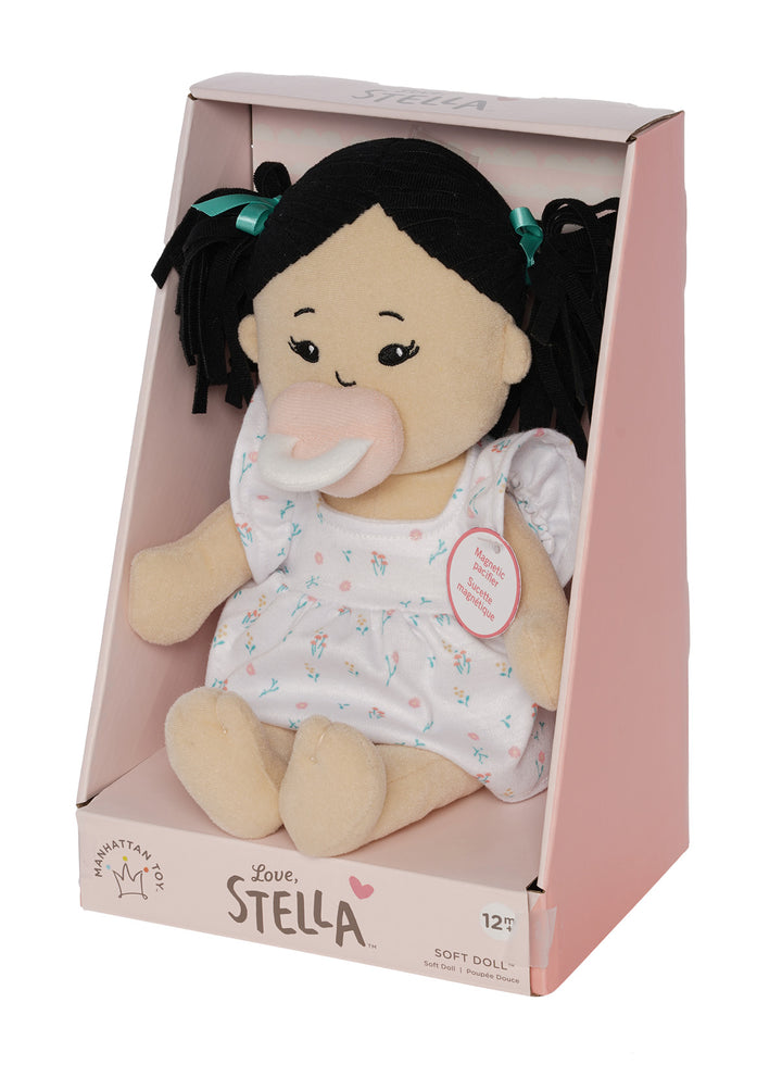 soft baby doll with light beige skin and black hair wearing a dress with a magnetic pacifier in open front box package