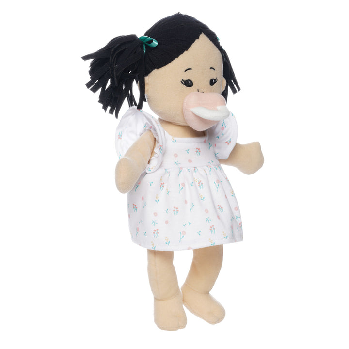 light beige soft doll with black pigtails in a dress seated with pink magnetic pacifier attached to the face