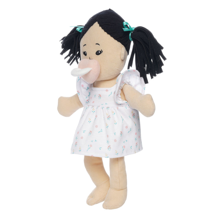 light beige soft doll with black pigtails in a dress seated with pink magnetic pacifier attached to the face