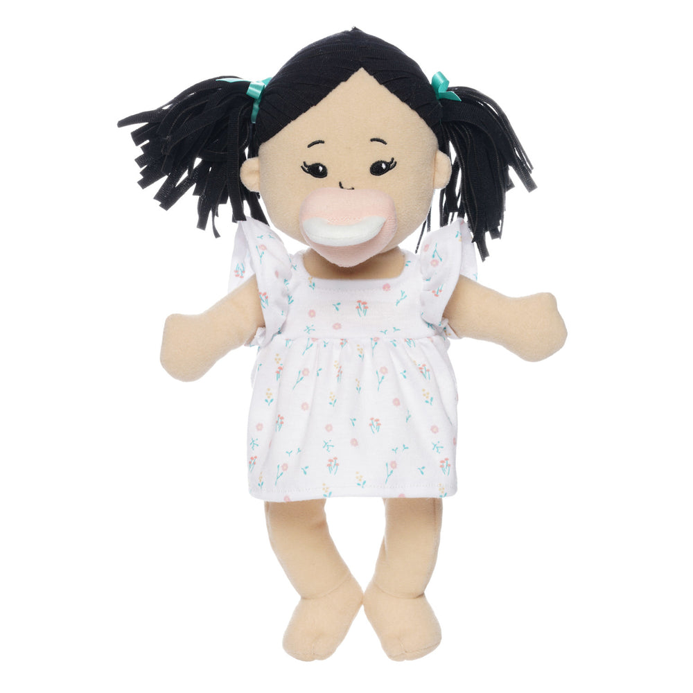 light beige soft doll with black pigtails in a dress seated with pink magnetic pacifier attached to the face