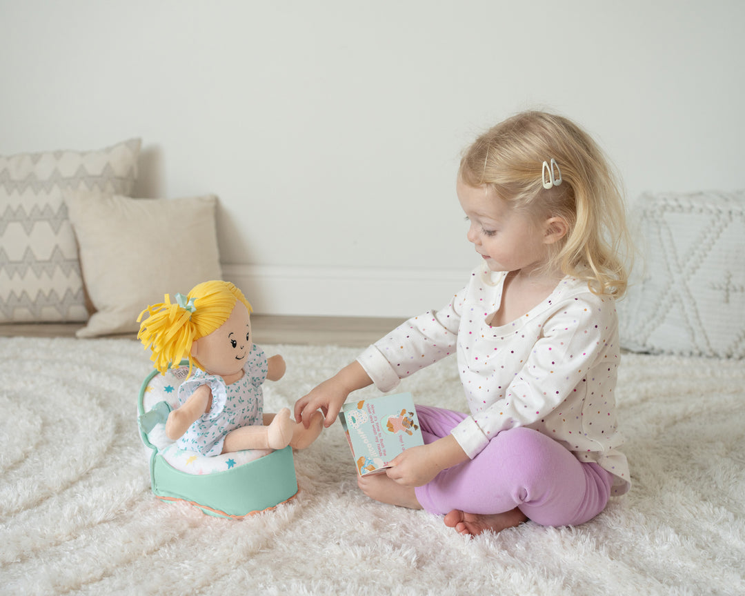 doll sized pretend potty with flushing sound with doll seated on the potty seated next to a toddler age girl reading the potty book to the doll.