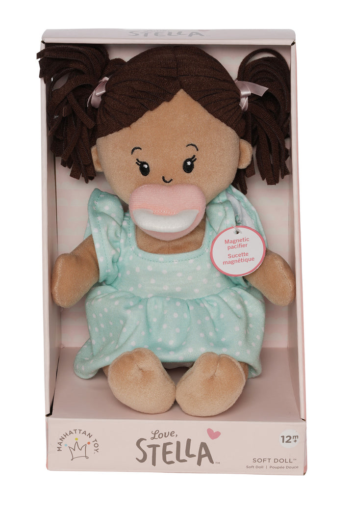 soft baby doll with beige skin and brown pigtails wearing a dress with a magnetic pacifier in open front box package