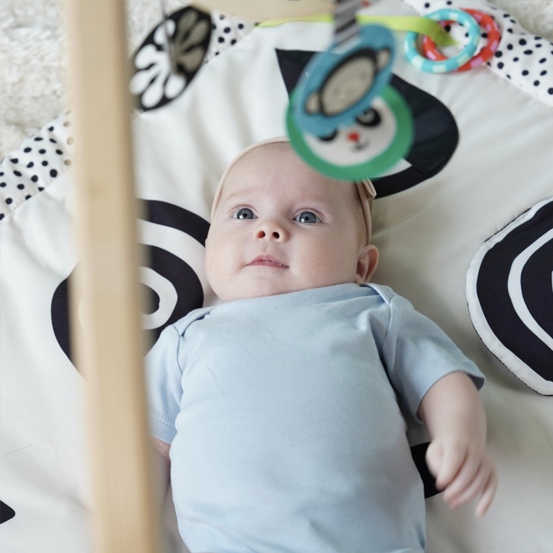 Baby laying on play mat looking up at a colorful mobile.