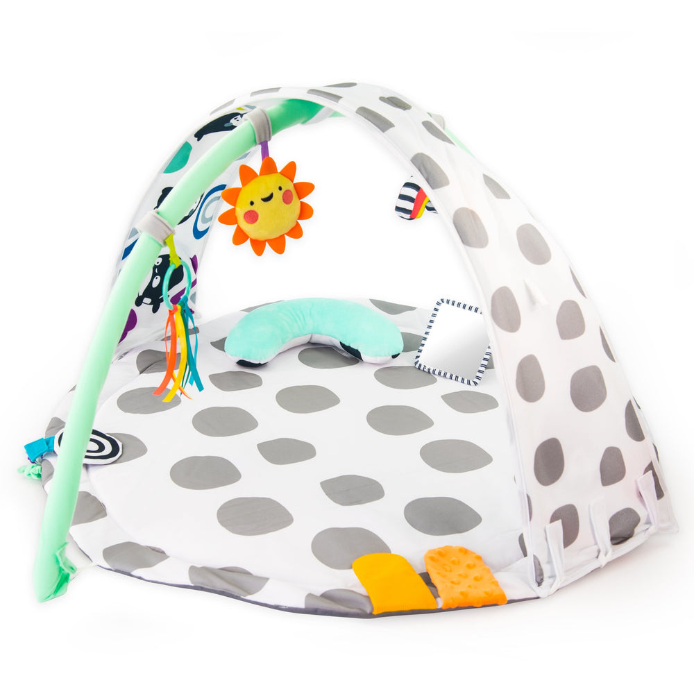 playmat with gray polka-dots, an arch with toys on it, a bolster, and floor mirror