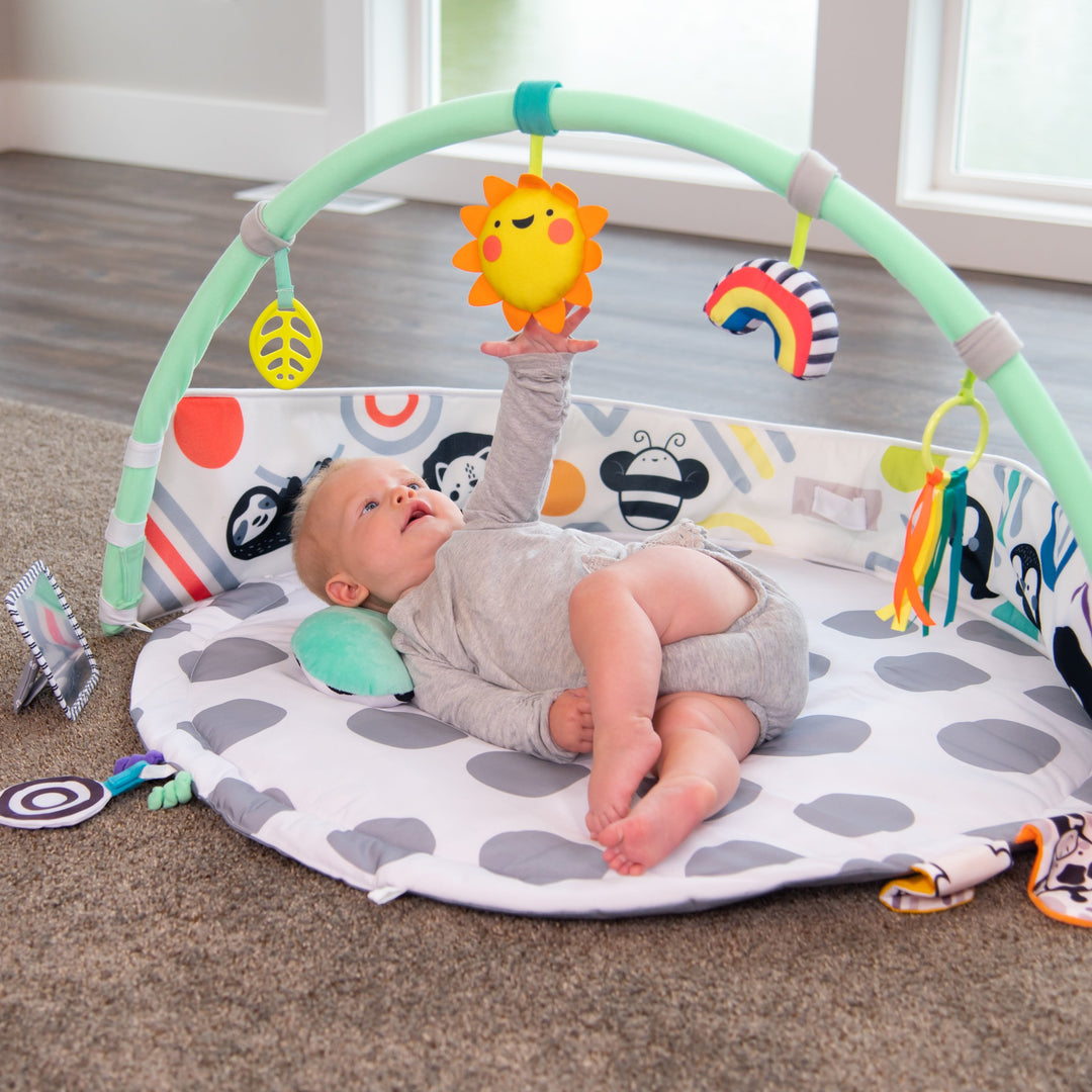 playmat with gray polka-dots, an arch with toys on it, a bolster, and floor mirror