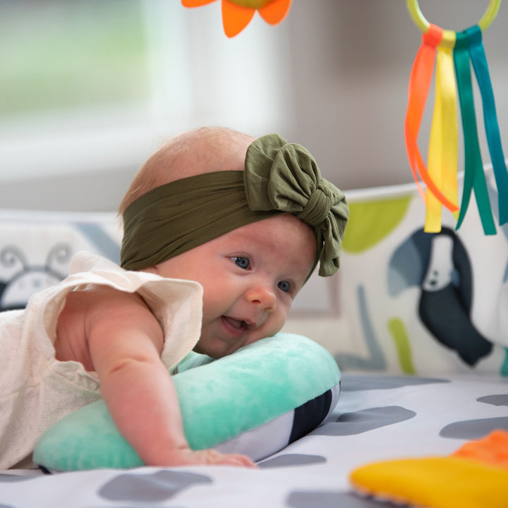 playmat with gray polka-dots, an arch with toys on it, a bolster, and floor mirror