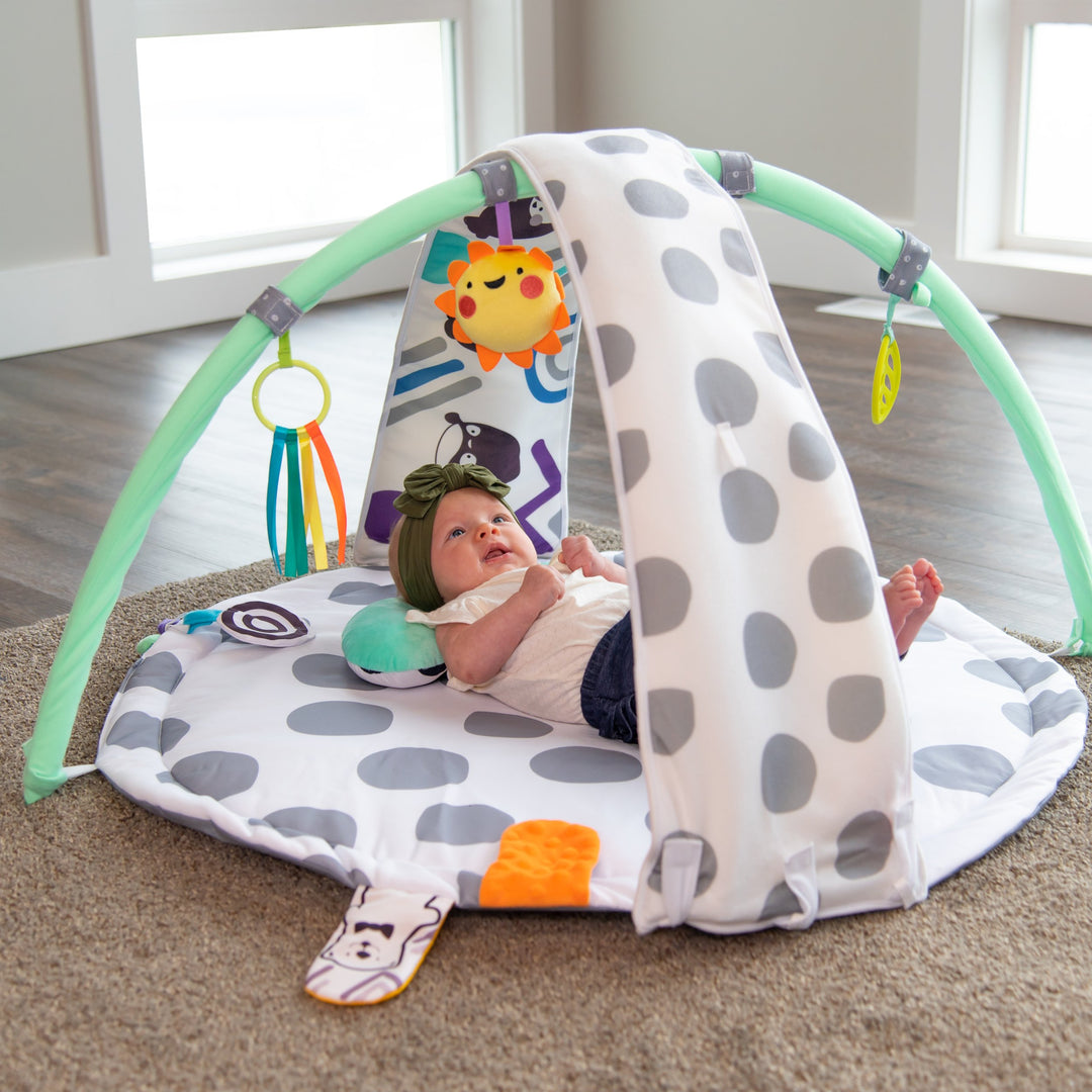 playmat with gray polka-dots, an arch with toys on it, a bolster, and floor mirror